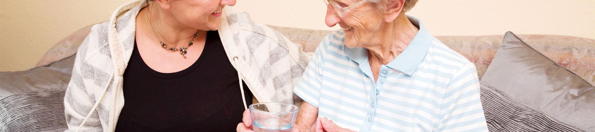 an older person holding a glass of water sitting next to her carer