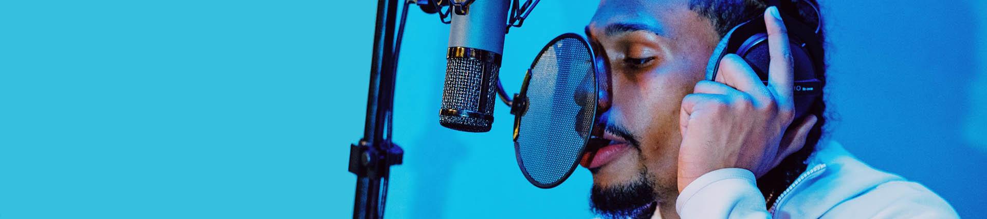 A singer records vocals in a recording studio using a pop shield in front of the mic