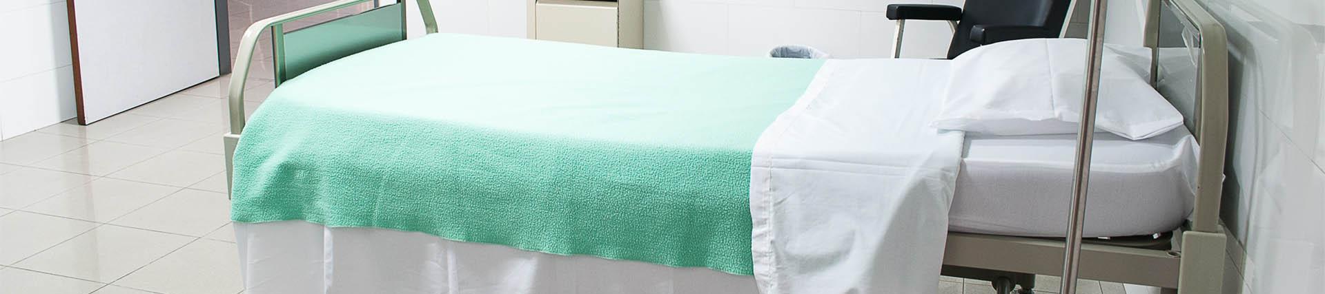 an empty hospital bed with a green blanket on it