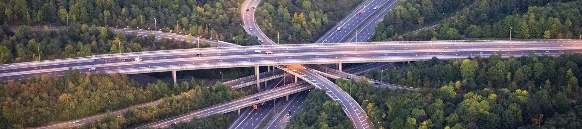 An M25 motorway interchange at dusk, the street lights are on and cars are travelling along the 4 layer elevated major road junction.