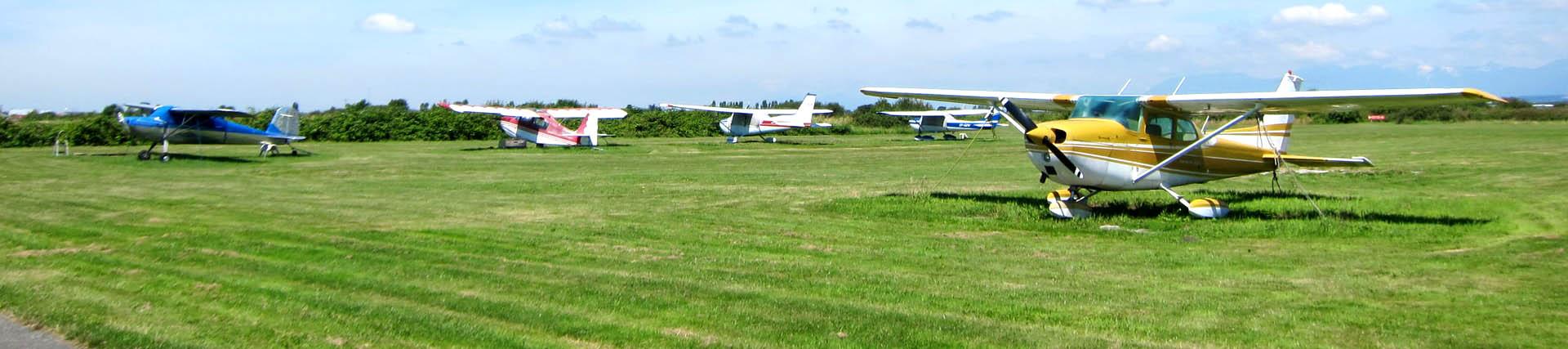Five brightly coloured Cessna 152 aeroplanes parked on grass on a sunny day 