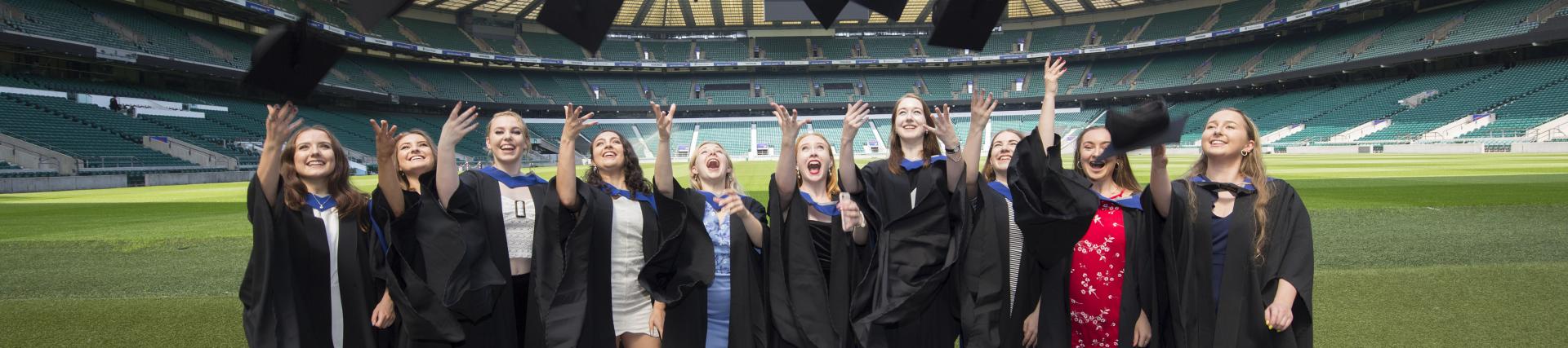 A group of graduates throwing their mortarboard hats in the air at Twickenham Stadium.