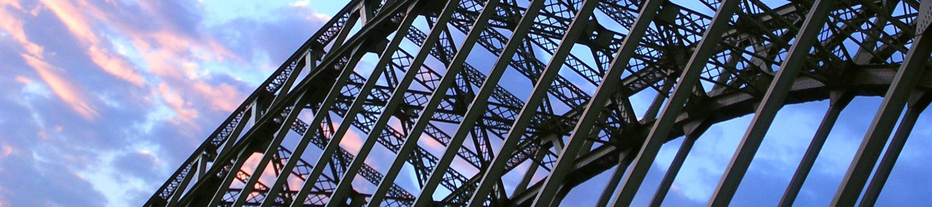 A curved iron bridge shot from below with a pink and blue sky in the background