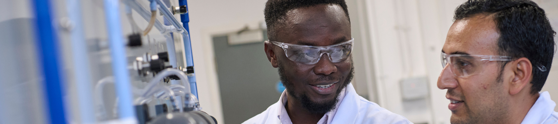 A student with a lecturer in a lab, wearing protective glasses.