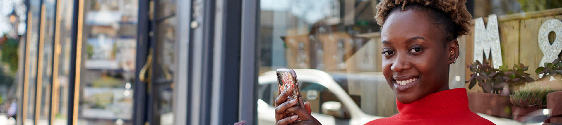 A student smiling outside of a cafe, holding her phone.