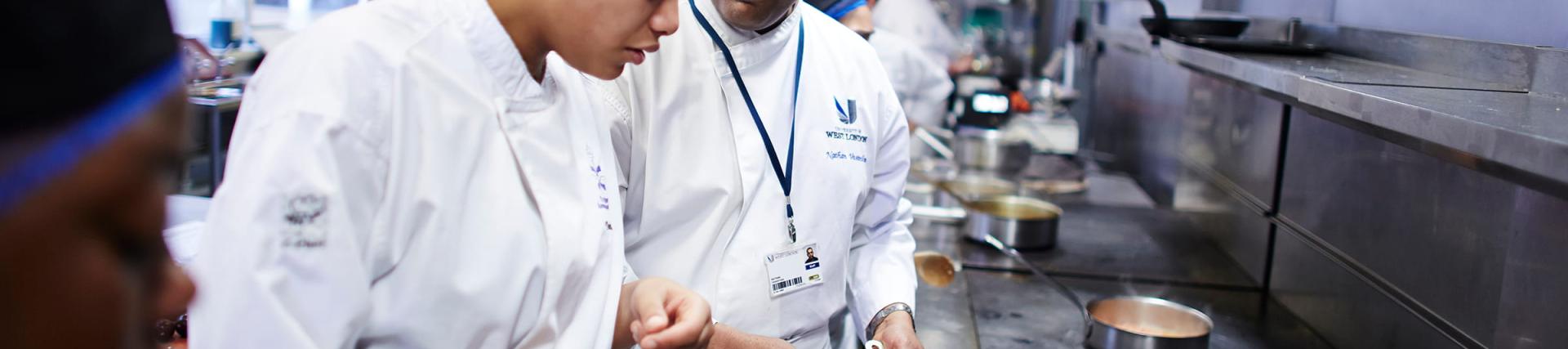 A male chef instructing a female student in Pillars Restaurant kitchen