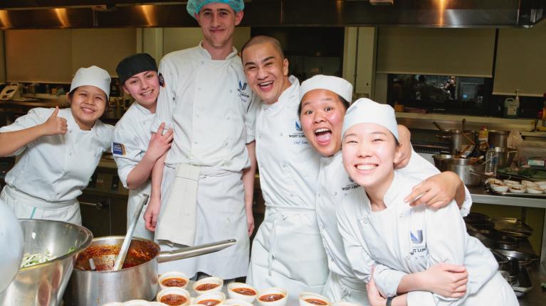 Chef Zam with students from UWL in the kitchen of Pillars restaurant, all wearing chef attire