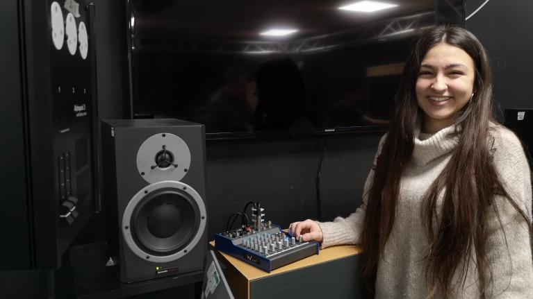 Music student posing in studio in front of mixer and stereo speakers.