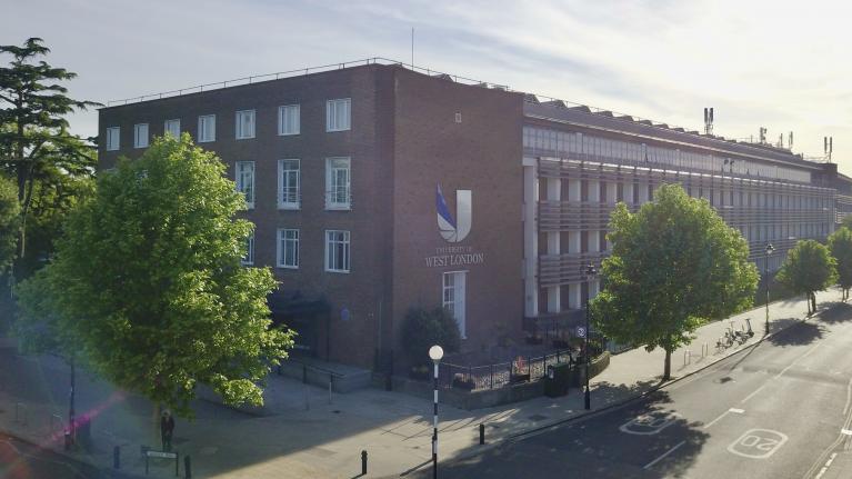 An image of the outside of campus from st Marys road, there are green trees lining the street and the UWL logo is on the side of the building.