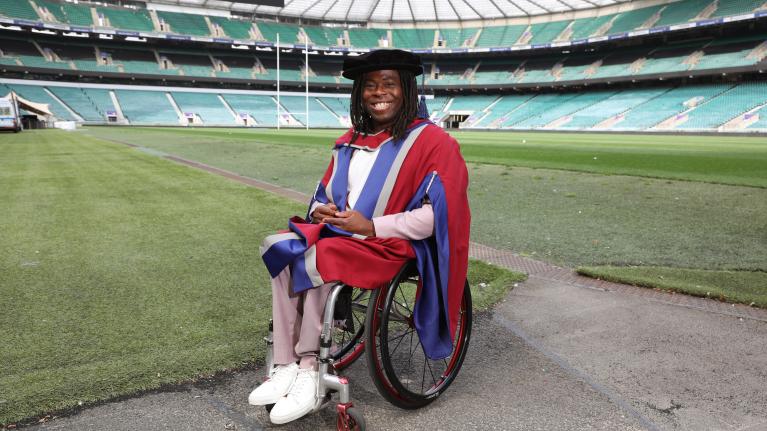 Ade Adepitan sat in his wheelchair celebrating his honorary degree pitchside at Twickenham Stadium.