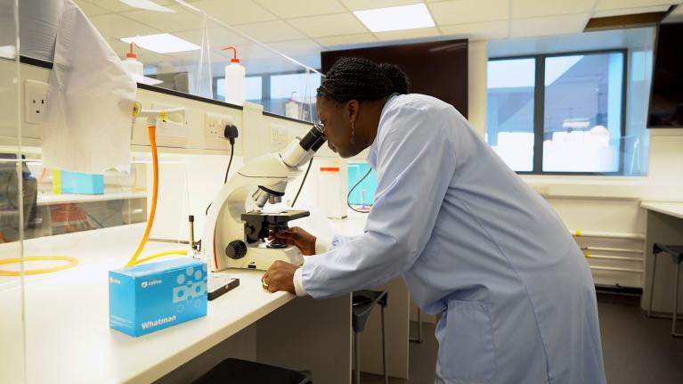 Dr Bernadine Idowu is using a microscope in a lab.