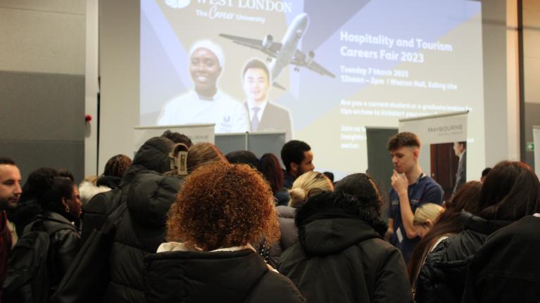 A slide projected onto the wall advertising the LGCHT Careers Fair 2023 on at UWL, with people surrounding.