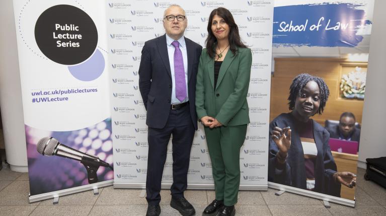 Lubna Shuja and Clive Coleman standing together at UWL in front of School of Law and Public Lectures Series banners.