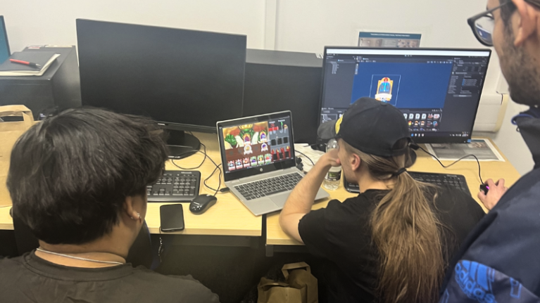 Students from the London School of Film, Media and Design and the London College of Music working together on a computer, developing a video game