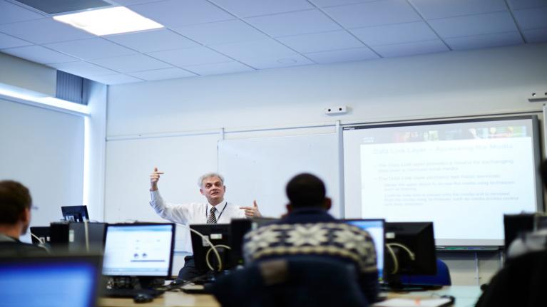 A male lecturer talking to students at computers